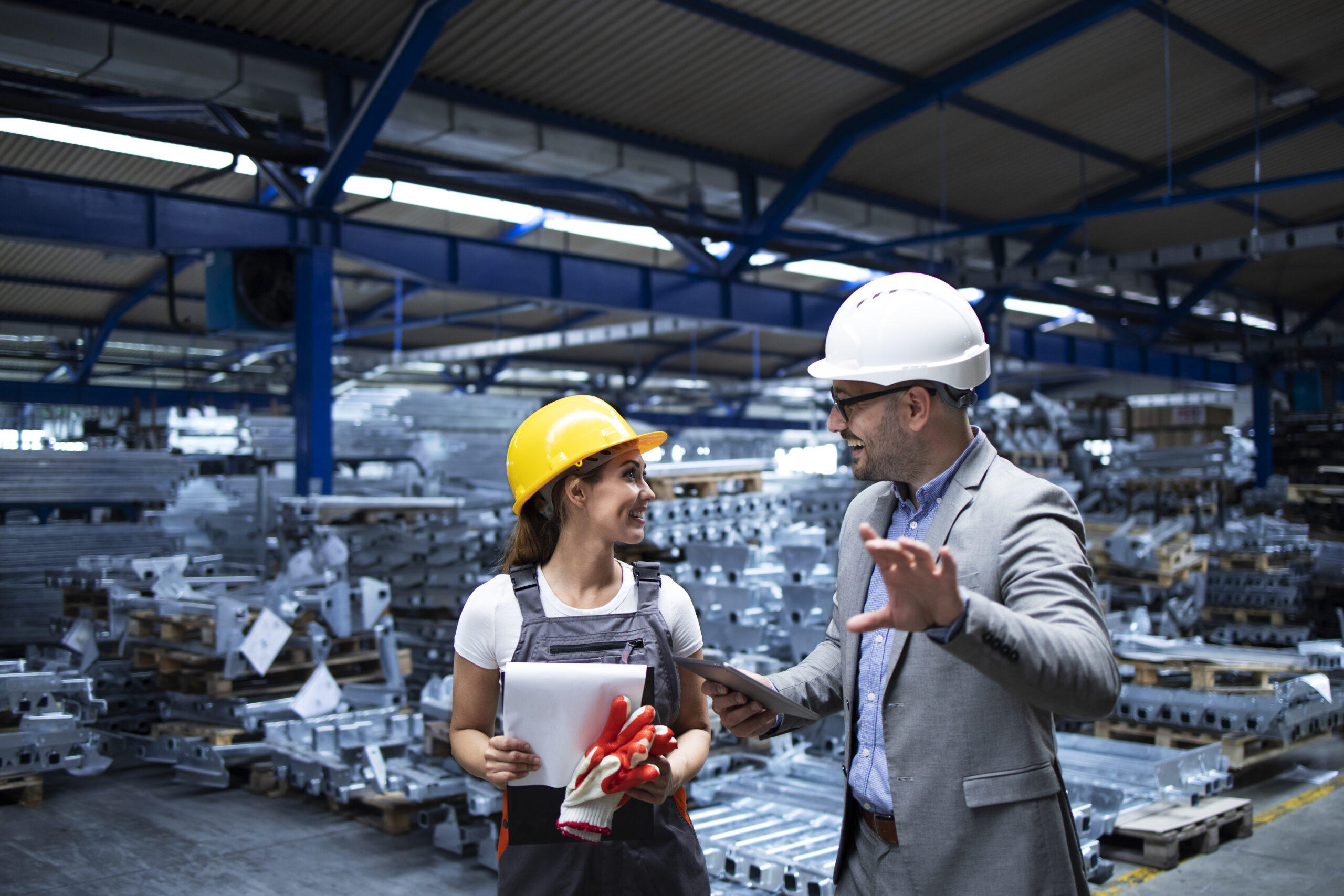 Manager wearing hardhat and industrial worker discussing about production in metal factory.